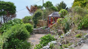 Un jardín con un mirador rojo, muros de piedra y diversas plantas.