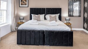 Ein Schlafzimmer mit einem großen Bett, zwei Nachttischen, einem Fenster mit Vorhängen und einem gerahmten Bild an der Wand.