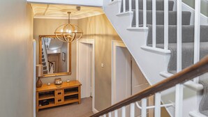 Eine Treppe mit weißen Geländern und einem hölzernen Handlauf, die zu einem Zwischenpodest mit einem Spiegel, einer Lampe und einem kleinen Tisch führt.