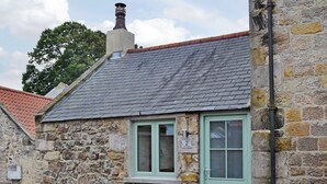 Un bâtiment en pierre avec une porte verte et une fenêtre sur laquelle est affiché un panneau indiquant « The Neuk ».