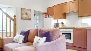 Ein Wohnzimmer mit einer Couch, einer Küchenzeile inklusive Schränke, Kühlschrank und Mikrowelle.