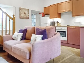 A living room with a sofa, a kitchen area with cabinets, a refrigerator, and a microwave.