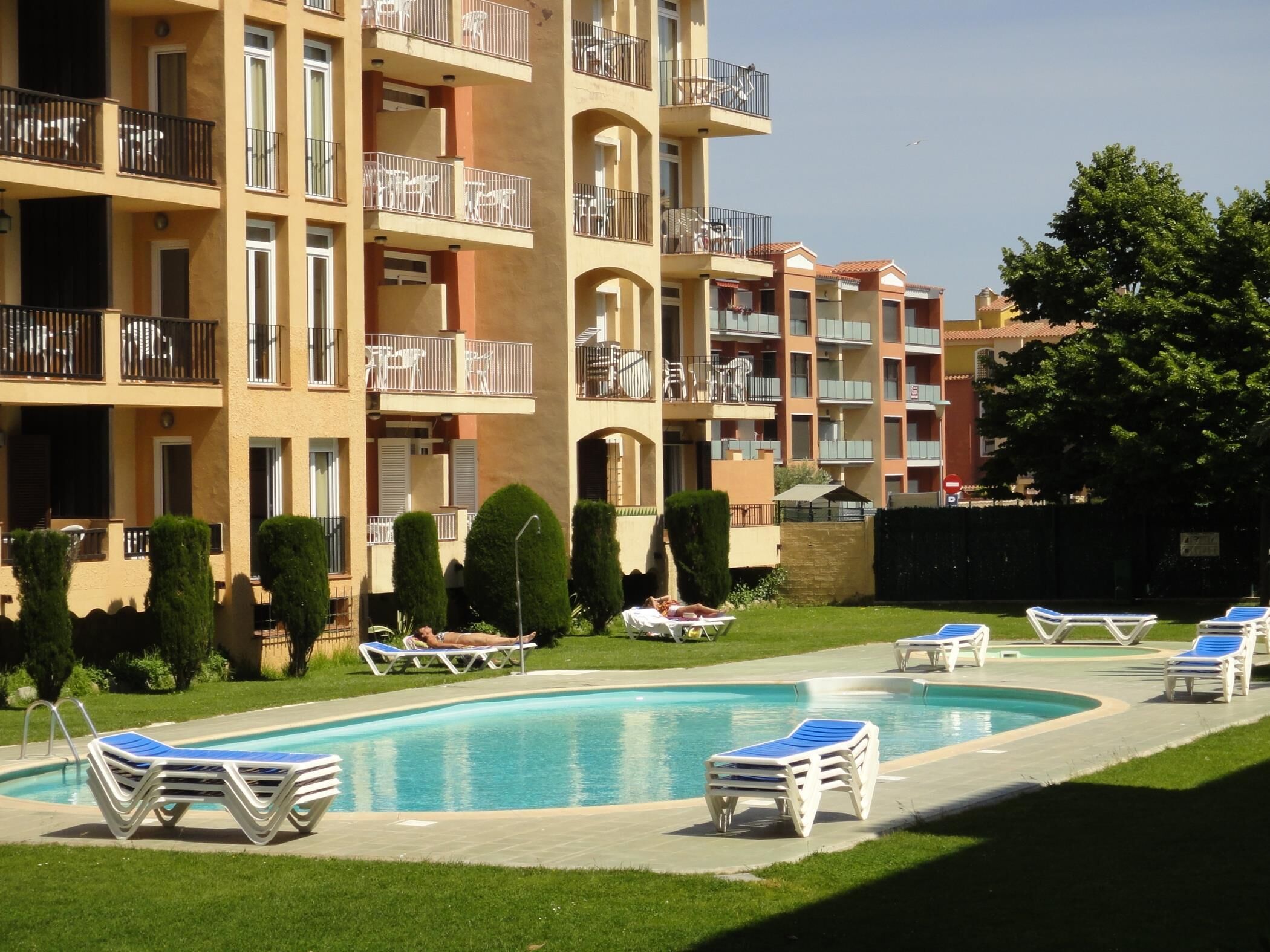 Zona de piscina con sillones de descanso y un edificio con varios balcones.