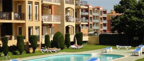 Zona de piscina con sillones de descanso y un edificio con varios balcones.