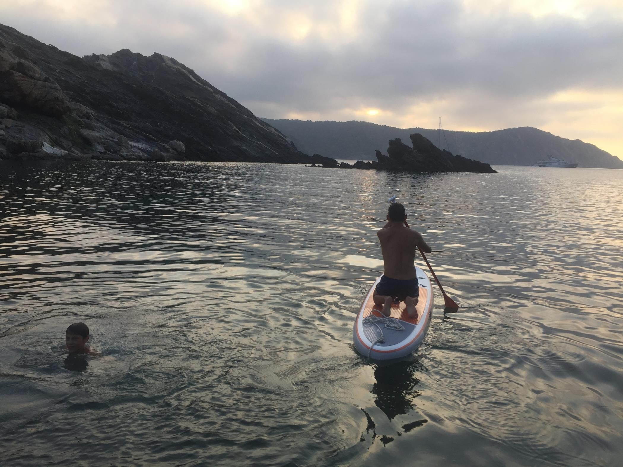 Une personne pratiquant le paddle sur une eau calme, avec une chaîne de montagnes en arrière-plan.