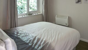 A bedroom with a bed, a window with curtains, a radiator, and wall art. - Westville by the Stream (Rosecraddoc, near Liskeard)