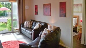 A living room with a black leather sofa, a red rug, and a dining area visible through a glass door. - Westville by the Stream (Rosecraddoc, near Liskeard)