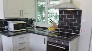 A modern kitchen with white cabinets, a black tiled backsplash, a microwave, a sink, and a stove. - Westville by the Stream (Rosecraddoc, near Liskeard)