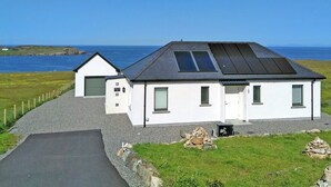 A white building with a sloped roof and a large window, located near a body of water. - 2 bedroom accommodation in Aird, near Stornoway (Aird, near Stornoway)