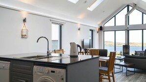 A modern kitchen with a built-in washing machine, a dining area with a view of the sea, and a cozy seating area with a fireplace. - 2 bedroom accommodation in Aird, near Stornoway (Aird, near Stornoway)