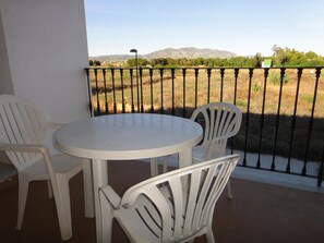 Ein Balkon mit rundem Tisch und zwei Stühlen, der Blick auf eine ländliche Landschaft mit Bergen und Bäumen bietet.