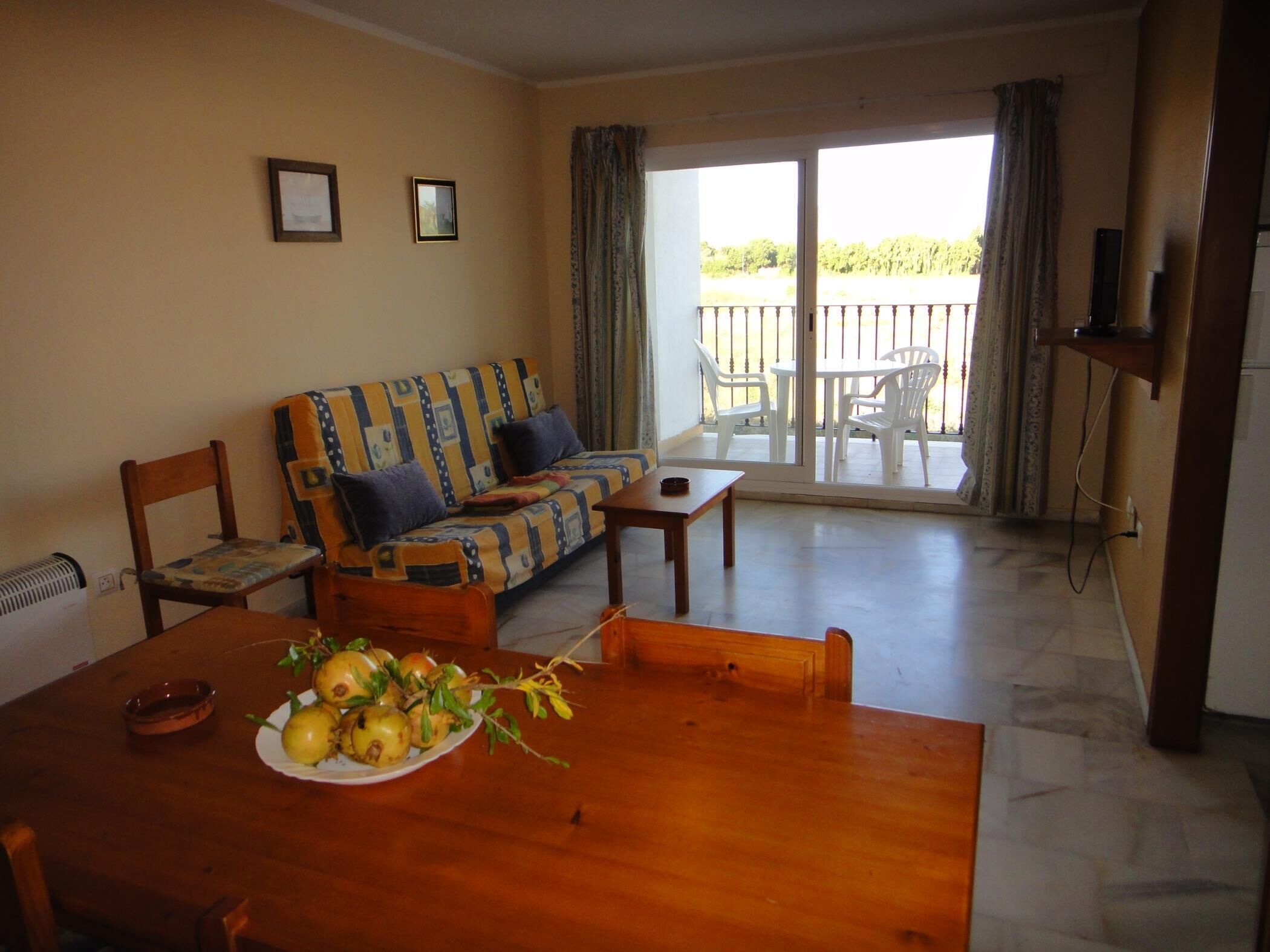 Una sala de estar con sofá, mesa de comedor y sillas. Hay un balcón con vistas a zonas verdes.