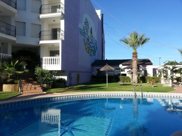 Ein Pool mit Sternenmuster, ein Gebäude mit Balkonen und eine Palme.