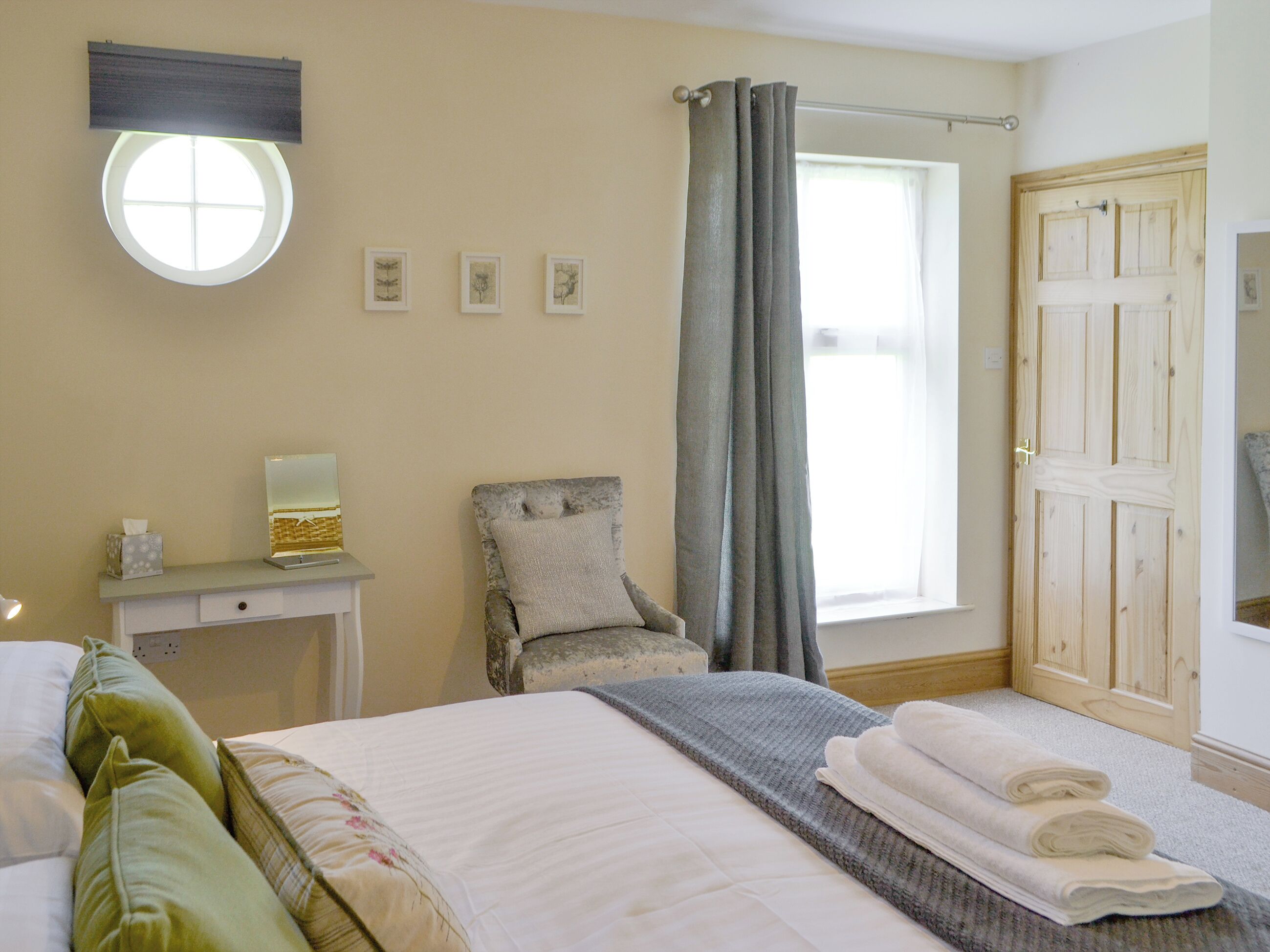 A bedroom with a bed, a chair, a desk, a window with curtains, and a door.