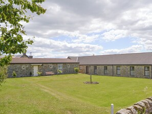 Un bâtiment en pierre avec un toit en tuiles, une cour verdoyante et un élément décoratif circulaire en pierre.