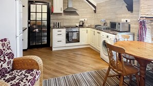 Une cuisine compacte équipée d’un four, d’un micro-ondes et d’un lave-linge intégrés, avec un plancher en bois et un coin repas comprenant une table et des chaises.