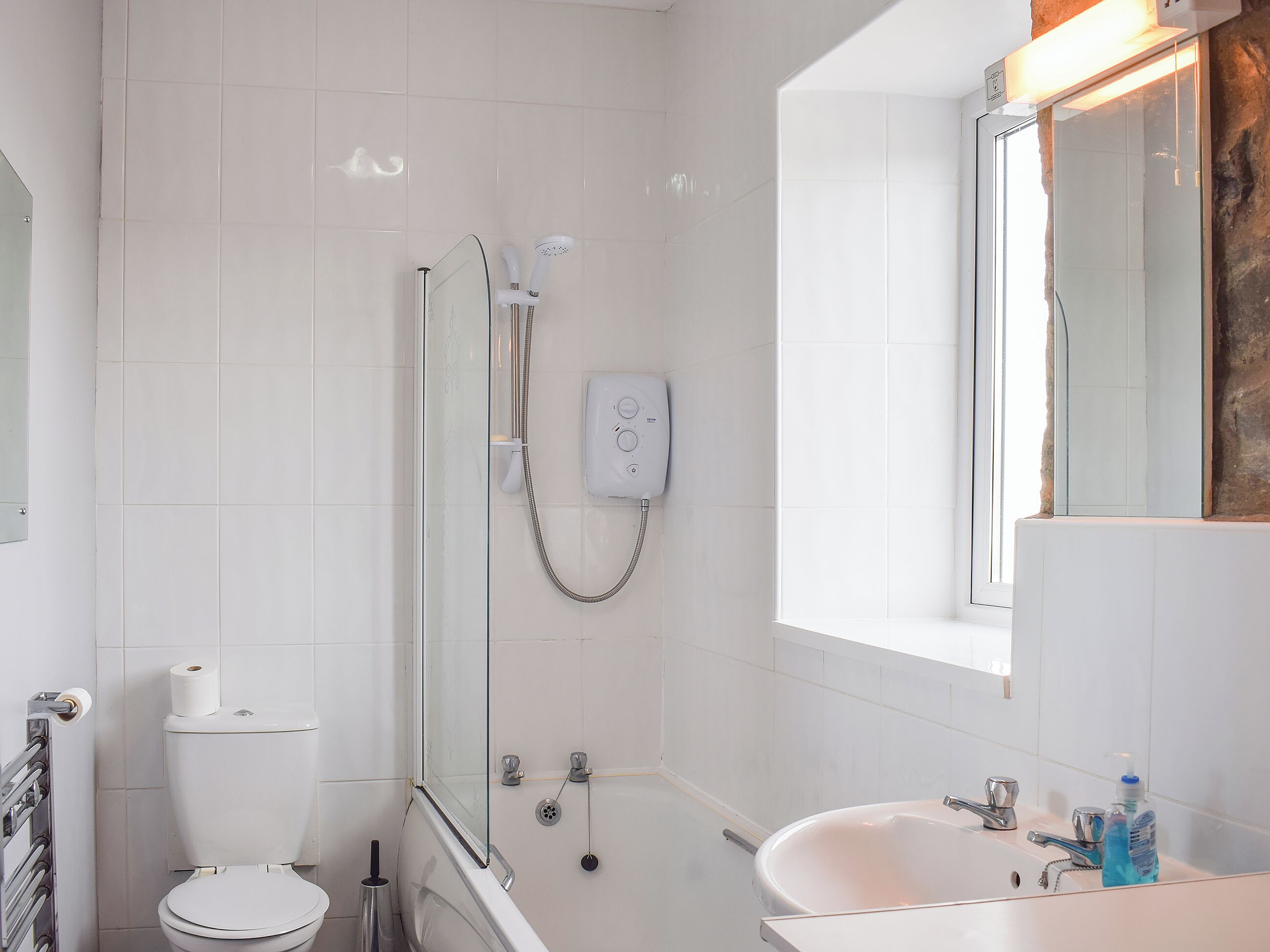 Un baño con inodoro, ducha con puerta de vidrio, bañera, lavamanos con espejo y ventana.