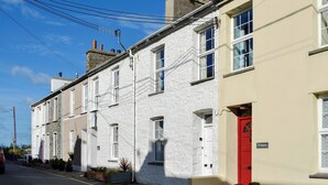 Una hilera de casas adosadas con fachadas blancas y color crema, una puerta roja y un cielo azul despejado.
