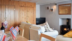 Una sala de estar acogedora con sofá, televisión, chimenea y comedor con mesa para dos.