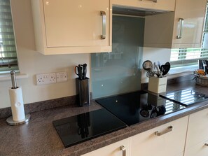 Cocina moderna con tope de inducción negro, armarios blancos y una ventana con persianas.