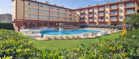 A hotel with a swimming pool, multiple balconies, and a well-maintained lawn.