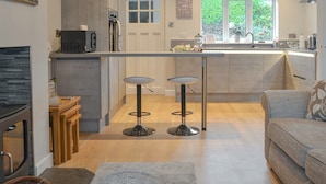 Een moderne keuken met een centraal eiland, twee barkrukken, een inbouwoven en een raam met uitzicht op groen.