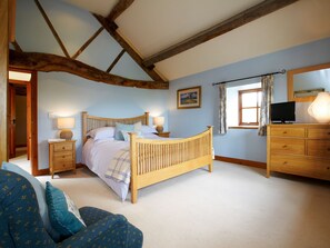 A bedroom with a wooden bed, bedside tables, a dresser, a television, and a window with curtains.