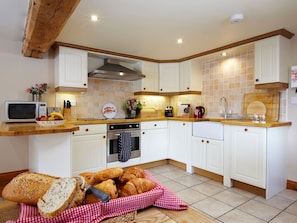 Una cocina con gabinetes blancos, microondas, estufa y diversos alimentos.