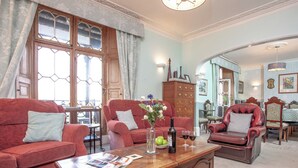 A spacious living room with a wooden coffee table, red sofas, and a dining area with a wooden cabinet and chairs. - 8 bedroom accommodation in Brixham (Brixham)