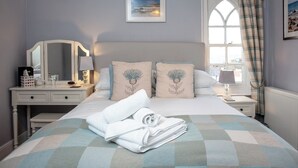 A neatly made bed with a checkered bedspread, a bedside table with a lamp, a mirror, and a framed picture on the wall. - 8 bedroom accommodation in Brixham (Brixham)