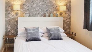 Un letto ben rifatto con lenzuola bianche e due cuscini decorati, un comodino con una lampada e un motivo floreale sulle pareti.
