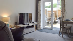 A living room with a sofa, a TV, a lamp, and a sliding glass door leading to an outdoor patio with a table and chairs. - 2 bedroom accommodation in Glossop (Glossop)