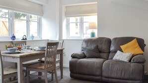 A dining area with a table set for four, a brown leather sofa, and a window with a view of the outside. - 2 bedroom accommodation in Glossop (Glossop)