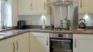 A modern kitchen with white cabinets, a stainless steel range hood, a gas stove, an oven, and a kettle. - 2 bedroom accommodation in Glossop (Glossop)