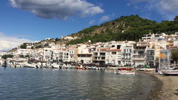 Une ville côtière avec des bâtiments le long du front de mer, des bateaux amarrés et un ciel dégagé.