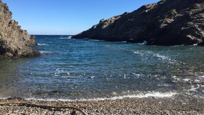 Une côte rocheuse bordée d’une eau d’un bleu limpide et d’une plage de galets.