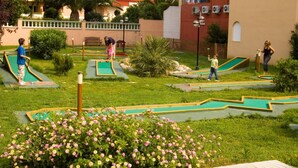 Un parcours de mini-golf comportant plusieurs trous, entouré de verdure et avec un bâtiment visible au fond.