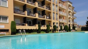 Une piscine à l’eau d’un bleu cristallin, entourée d’un immeuble à plusieurs étages doté de balcons et d’une façade recouverte de carreaux.