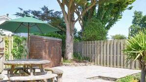 Eine Terrasse mit Holztisch und Bänken, einem grünen Sonnenschirm und einem Holzzaun.