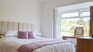 Een slaapkamer met een groot bed, een hoofdbord, een nachtkastje, een spiegel en een raam met uitzicht.