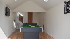 Une table de billard dans une pièce dotée d’un plancher en bois, d’une porte et d’un jeu de fléchettes accroché au mur.