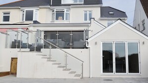 Een modern huis met twee verdiepingen, een glazen conservatorium, een trap en een garage.