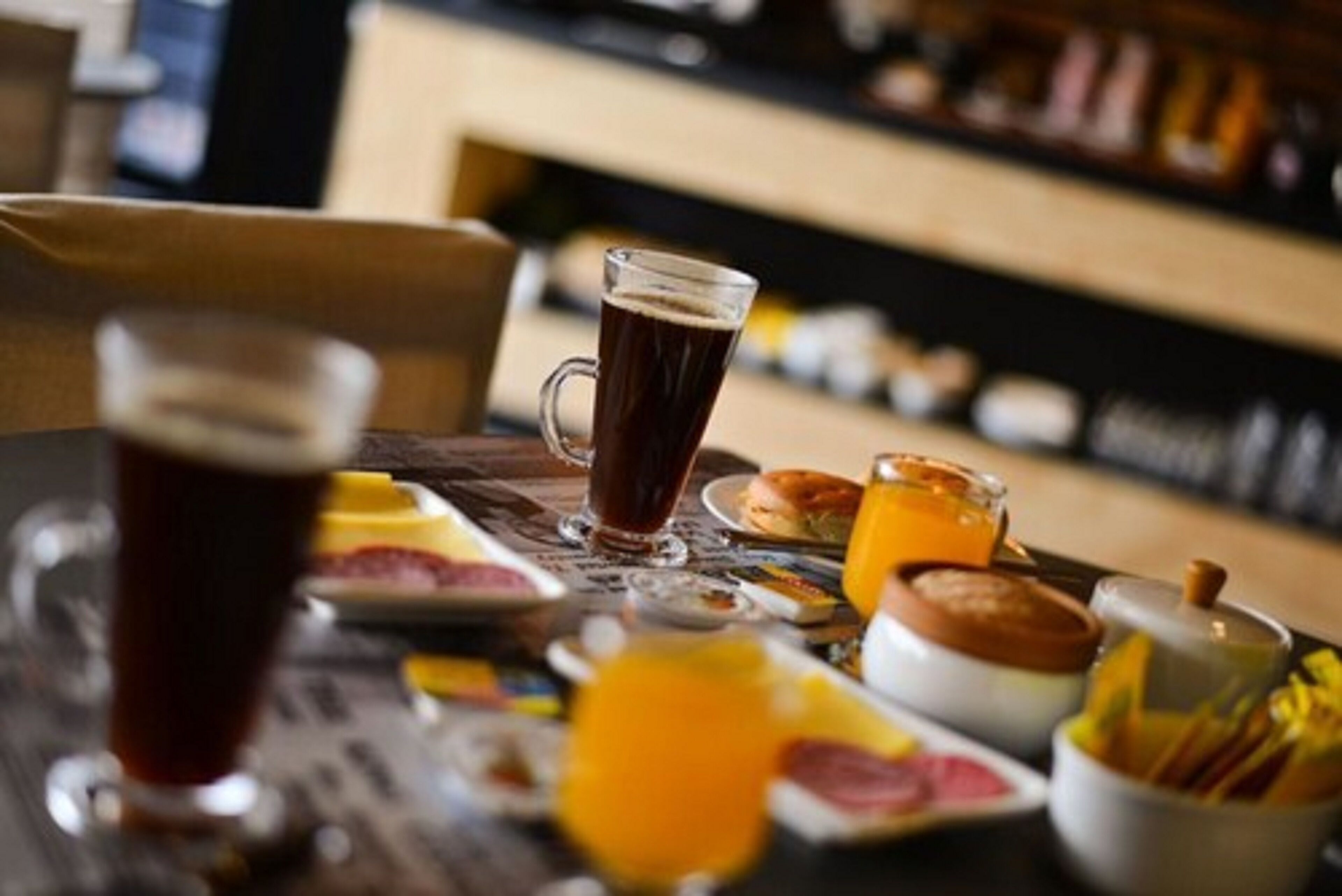 A breakfast setting with a glass of dark liquid, possibly coffee or tea, and a glass of orange juice on a table with various breakfast items.