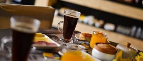 A breakfast setting with a glass of dark liquid, possibly coffee or tea, and a glass of orange juice on a table with various breakfast items.