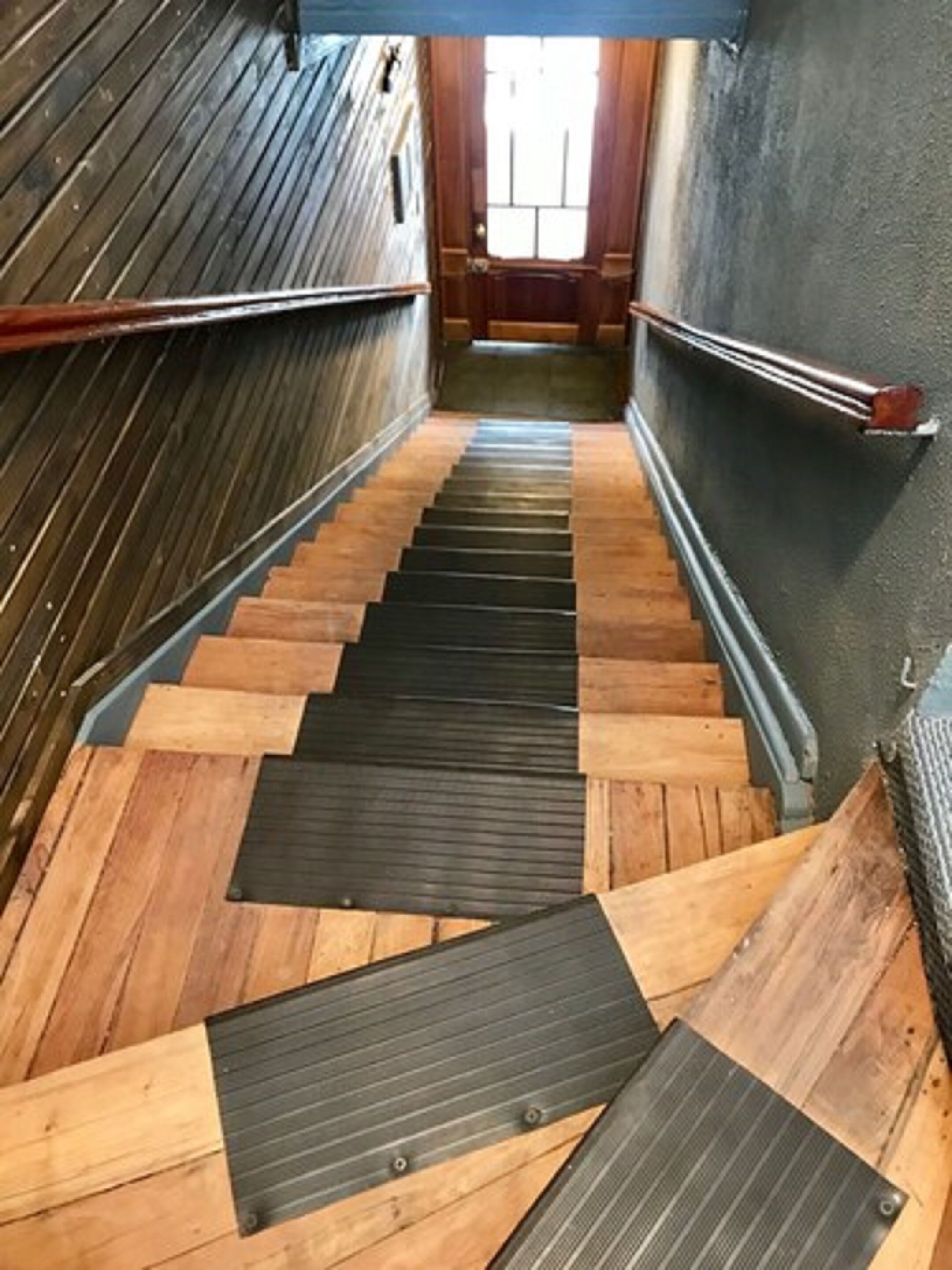 Una escalera de madera con peldaños negros antideslizantes que conduce a una puerta.