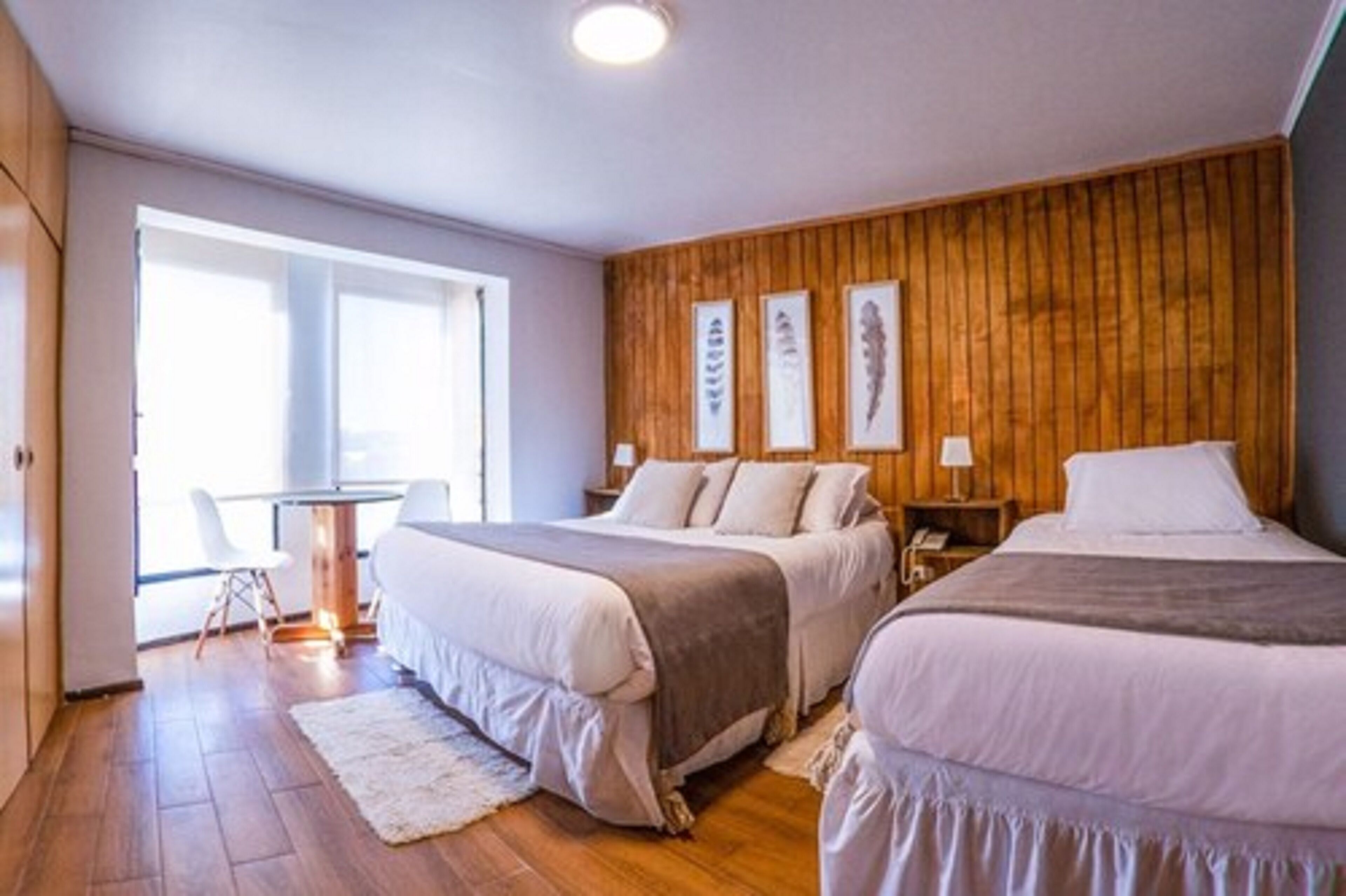 Un dormitorio con dos camas, una pared de madera y un escritorio con sillas.
