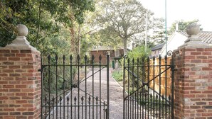 A gated entrance with a gravel path leading to a brick building. - The Old Rectory Cottage (Tothill, near Louth)