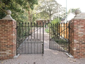 A gated entrance with a gravel path leading to a brick building. - The Old Rectory Cottage (Tothill, near Louth)