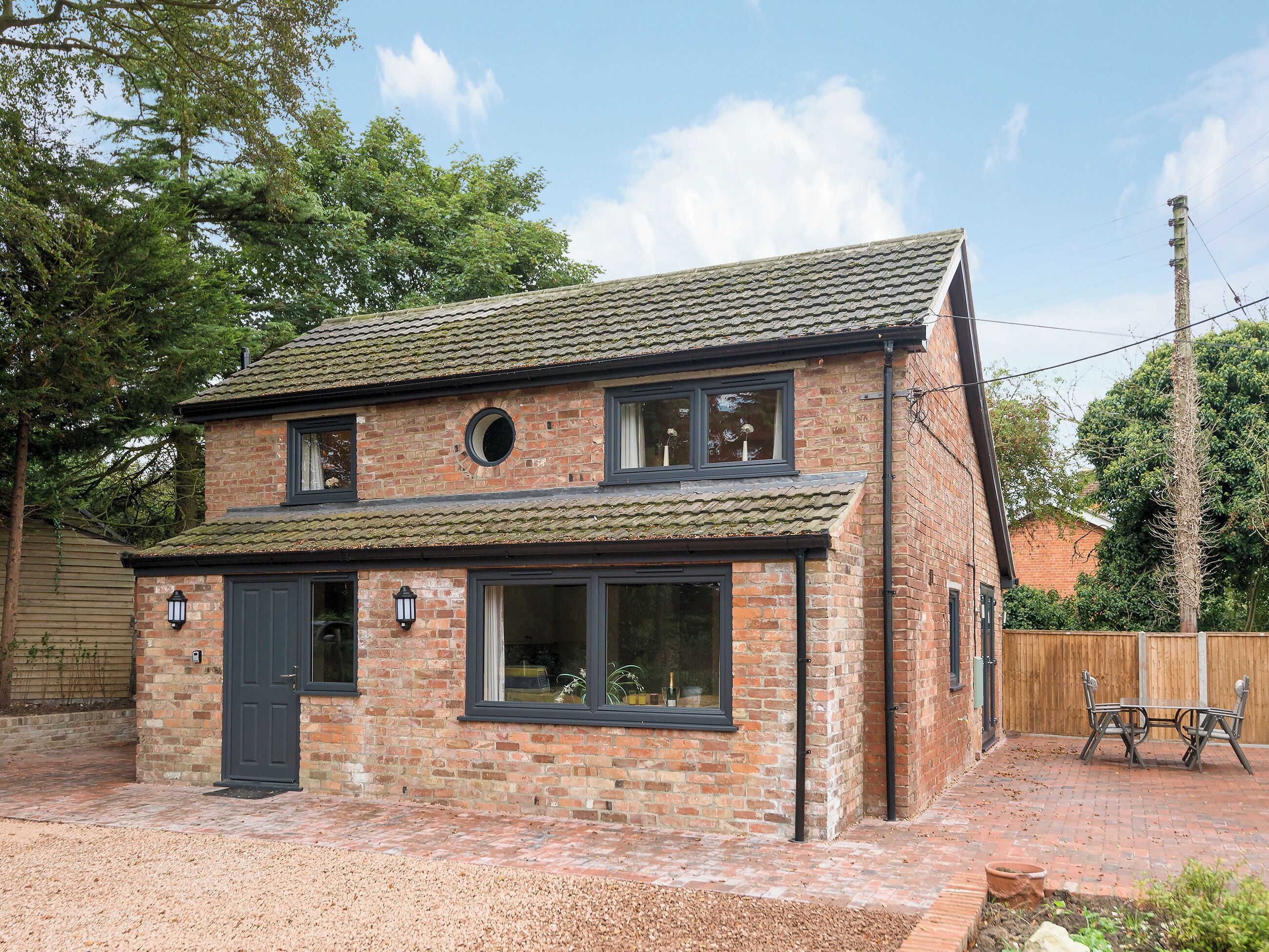 A two-story brick house with a tiled roof, a front door, and a small circular window.