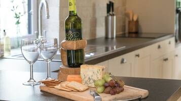 Una encimera de cocina con una botella de vino, dos copas, queso, galletas y uvas.